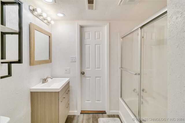 bathroom featuring enclosed tub / shower combo, vanity, wood-type flooring, and a textured ceiling