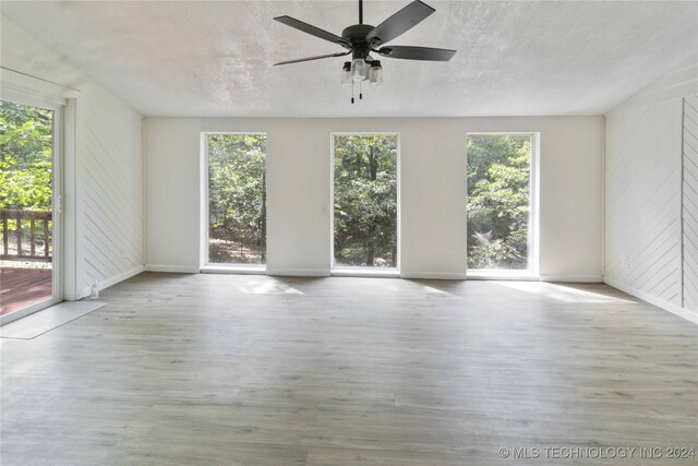 unfurnished room with ceiling fan, light hardwood / wood-style floors, a textured ceiling, and wooden walls