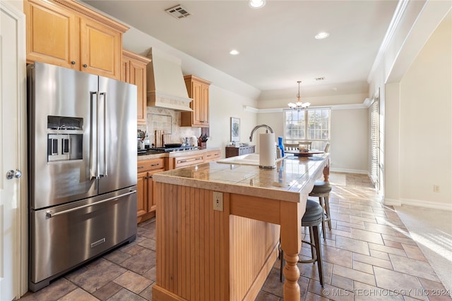 kitchen with backsplash, high quality fridge, custom range hood, a kitchen island with sink, and sink