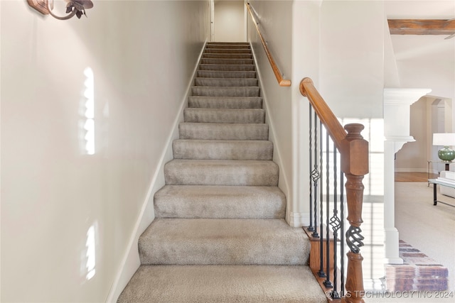 stairs with carpet and beamed ceiling