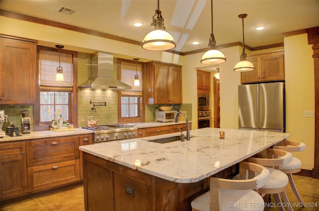 kitchen featuring sink, wall chimney range hood, backsplash, a center island with sink, and appliances with stainless steel finishes