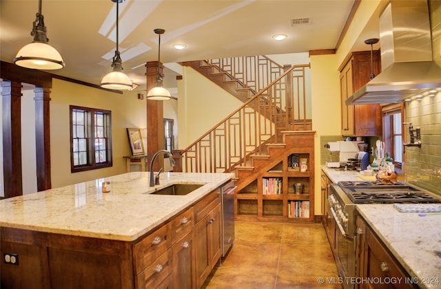 kitchen with sink, wall chimney exhaust hood, hanging light fixtures, tasteful backsplash, and a kitchen island with sink