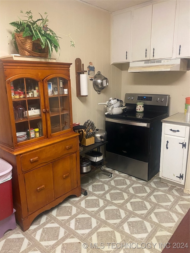 kitchen with white cabinets, stainless steel electric range oven, and wood walls