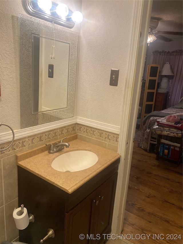 bathroom featuring ceiling fan, hardwood / wood-style floors, vanity, and tile walls