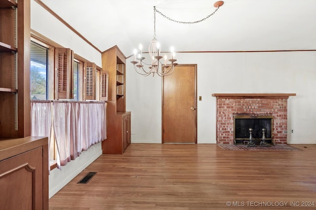 unfurnished living room featuring hardwood / wood-style floors, crown molding, a fireplace, and an inviting chandelier