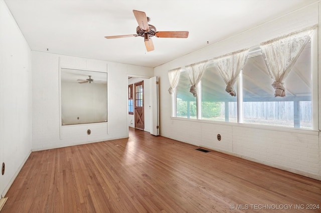 spare room with ceiling fan, hardwood / wood-style floors, and brick wall