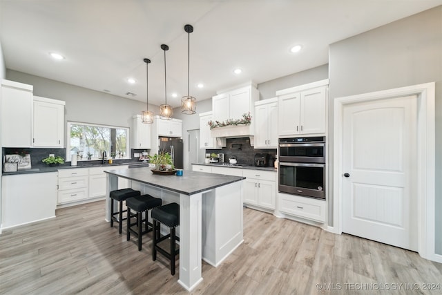 kitchen with white cabinets, light hardwood / wood-style flooring, a kitchen island, and appliances with stainless steel finishes