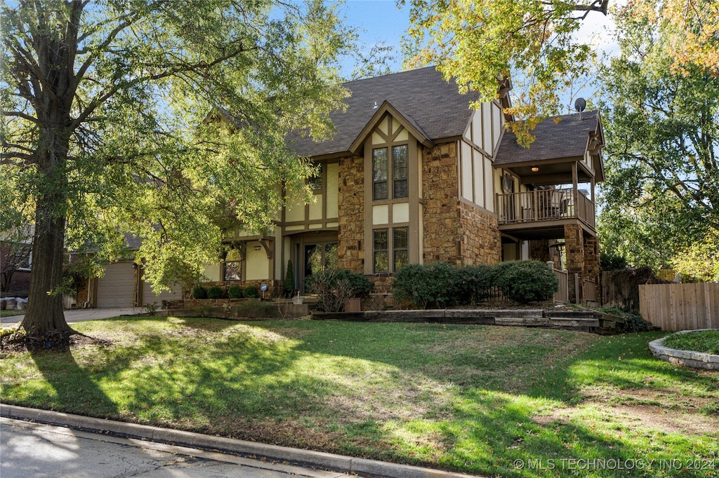 tudor home featuring a balcony, a garage, and a front lawn