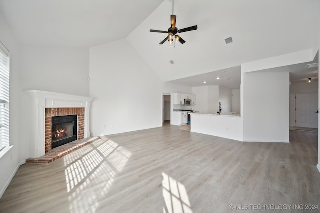 unfurnished living room with visible vents, ceiling fan, light wood-style flooring, a fireplace, and high vaulted ceiling