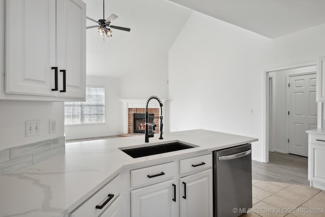 kitchen with a sink, white cabinets, a brick fireplace, ceiling fan, and dishwasher