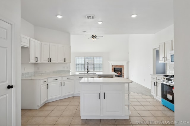 kitchen with a ceiling fan, gas stove, white microwave, a sink, and a brick fireplace