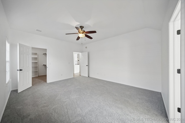 unfurnished bedroom with a walk in closet, lofted ceiling, carpet floors, baseboards, and ceiling fan