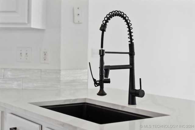 interior details with white cabinetry, decorative backsplash, and a sink