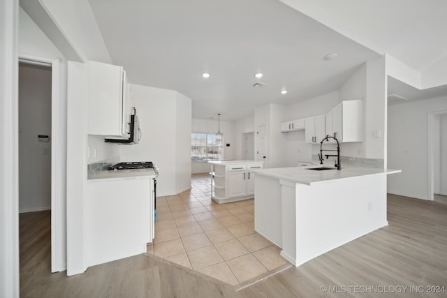 kitchen featuring white gas range, white cabinets, a peninsula, and a sink