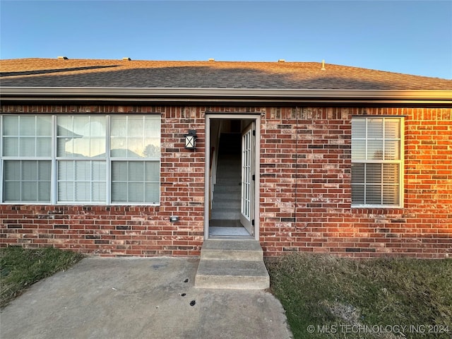 view of exterior entry with brick siding and roof with shingles