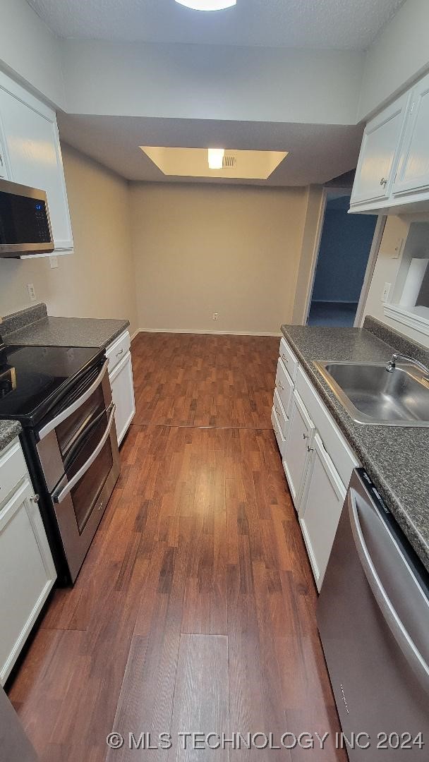 kitchen with dark countertops, a sink, stainless steel appliances, and dark wood finished floors