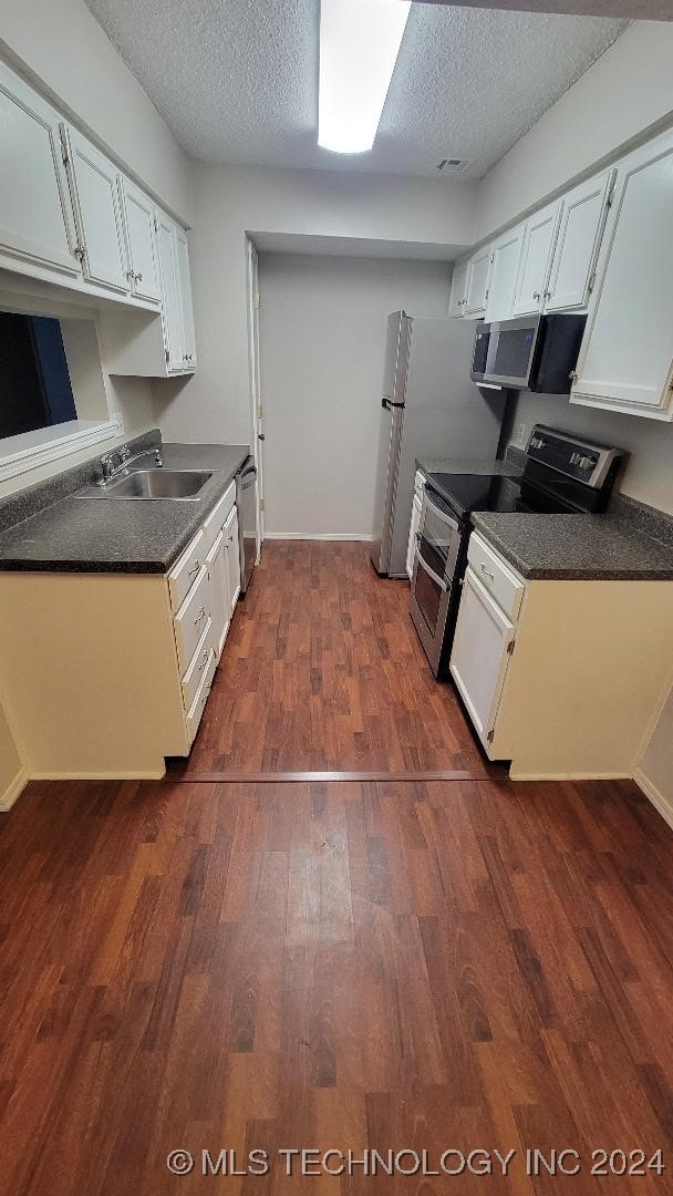 kitchen with a sink, stainless steel appliances, dark wood-type flooring, dark countertops, and a textured ceiling