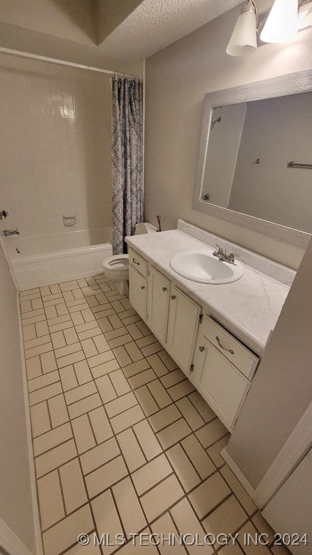 bathroom featuring shower / bath combo with shower curtain, vanity, toilet, and a textured ceiling
