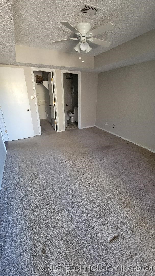 unfurnished bedroom with a textured ceiling, visible vents, a ceiling fan, and carpet floors
