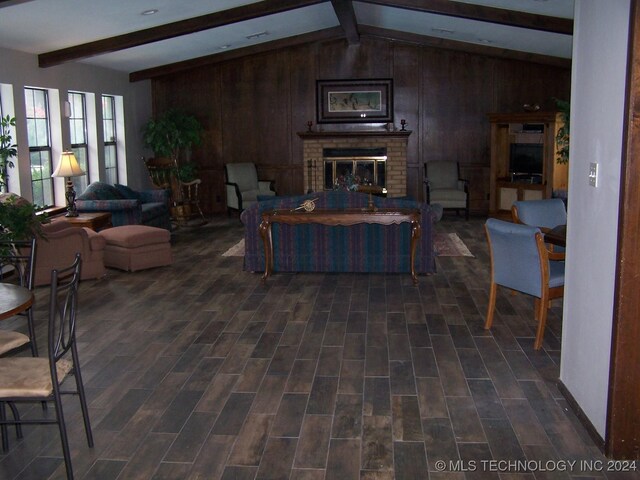 living area featuring dark wood finished floors, vaulted ceiling with beams, wooden walls, and a fireplace