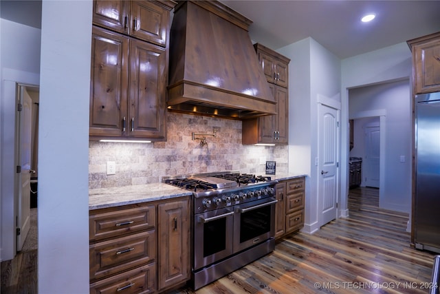 kitchen featuring light stone countertops, tasteful backsplash, custom exhaust hood, high end appliances, and dark wood-type flooring