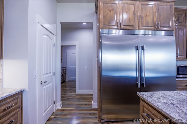 kitchen with light stone countertops, stainless steel appliances, and dark wood-type flooring