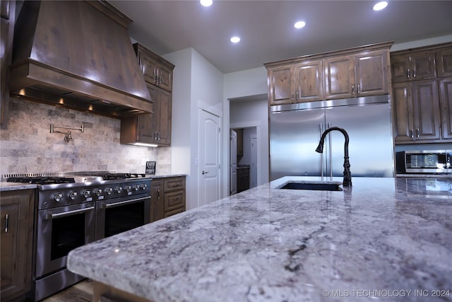 kitchen featuring backsplash, light stone counters, custom exhaust hood, premium appliances, and hardwood / wood-style flooring