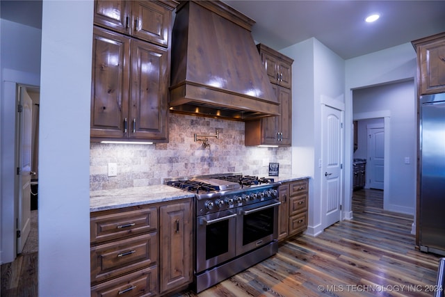 kitchen featuring high quality appliances, dark wood-type flooring, decorative backsplash, light stone countertops, and custom range hood