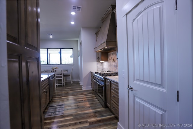 kitchen featuring appliances with stainless steel finishes, dark hardwood / wood-style flooring, tasteful backsplash, custom range hood, and dark brown cabinetry