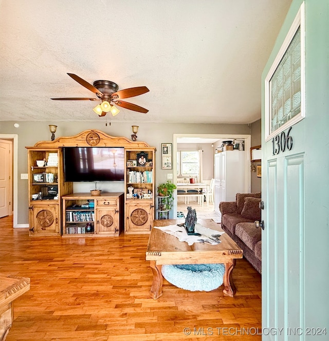 living room with a textured ceiling, light wood-type flooring, and ceiling fan