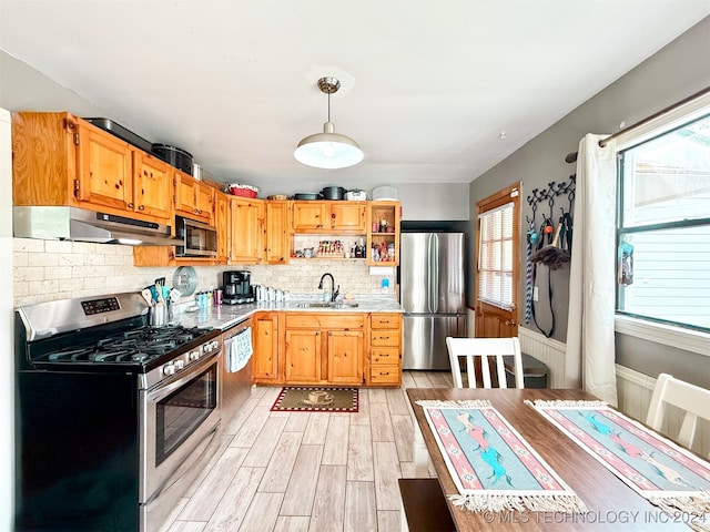 kitchen featuring sink, hanging light fixtures, backsplash, light hardwood / wood-style floors, and appliances with stainless steel finishes