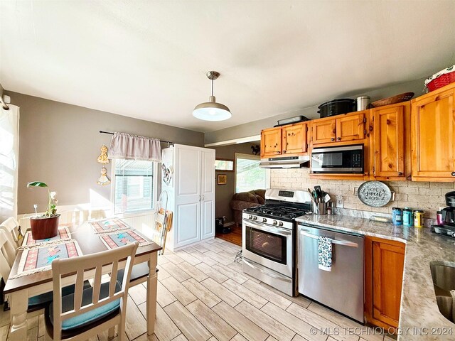 1306 E Comanche Ave, Mcalester, OK 74501 - kitchen featuring appliances with stainless steel finishes, tasteful backsplash, under cabinet range hood, light wood finished floors, and brown cabinetry