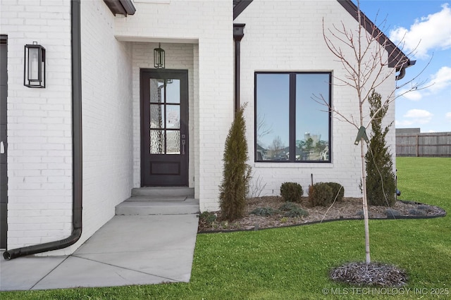 property entrance with a yard, brick siding, and fence