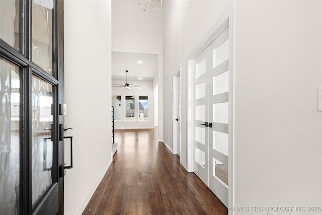 hallway featuring a towering ceiling, dark wood-style flooring, baseboards, recessed lighting, and french doors