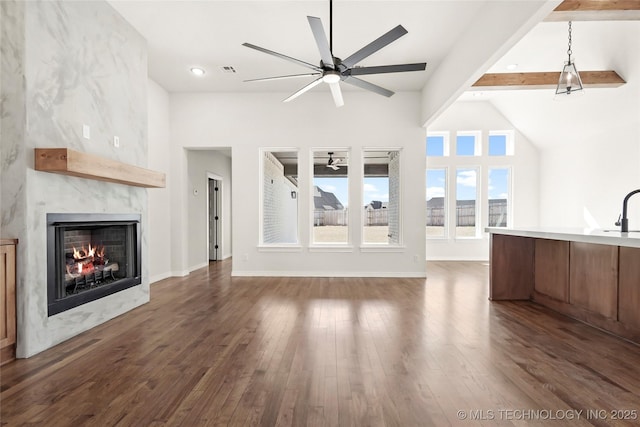 unfurnished living room with ceiling fan, beamed ceiling, dark wood-type flooring, a sink, and a premium fireplace