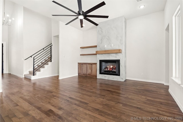 unfurnished living room featuring baseboards, ceiling fan, a high end fireplace, stairway, and dark wood-type flooring