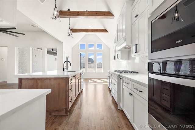 kitchen featuring a sink, a ceiling fan, dark wood-type flooring, a center island with sink, and vaulted ceiling with beams