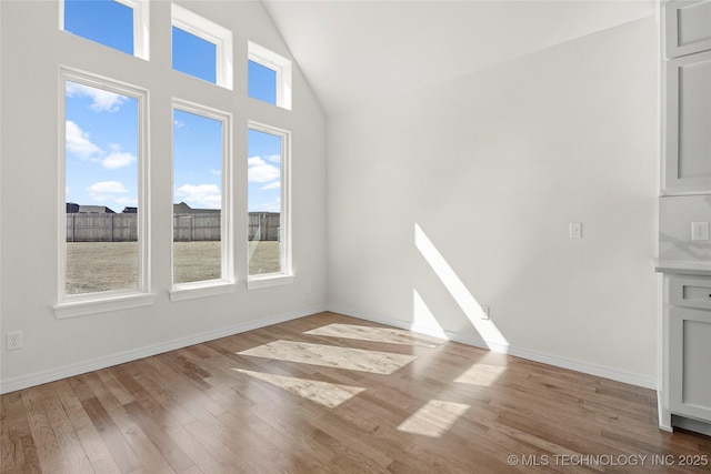 interior space with baseboards, high vaulted ceiling, and wood finished floors