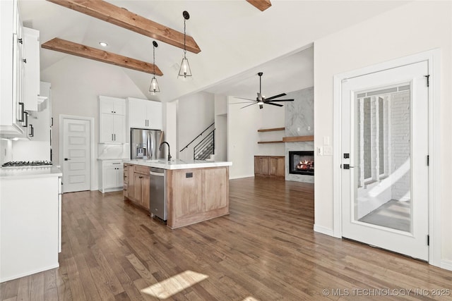 kitchen with a ceiling fan, a kitchen island with sink, beamed ceiling, stainless steel appliances, and wood finished floors