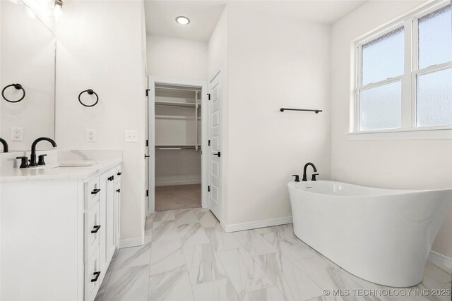 bathroom with a freestanding tub, vanity, baseboards, a spacious closet, and marble finish floor
