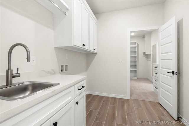 clothes washing area featuring baseboards, washer hookup, a sink, light wood-style floors, and cabinet space