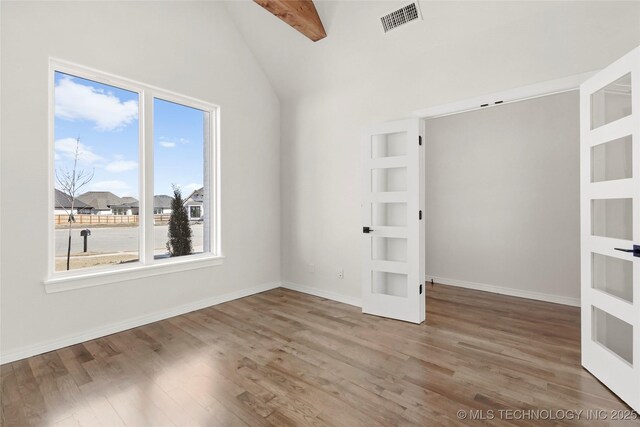 empty room with vaulted ceiling with beams, french doors, visible vents, and wood finished floors