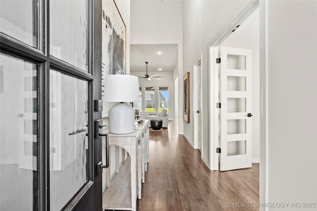 hall featuring a high ceiling, wood finished floors, baseboards, and recessed lighting