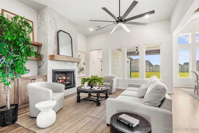 living area with recessed lighting, light wood finished floors, a premium fireplace, and a ceiling fan