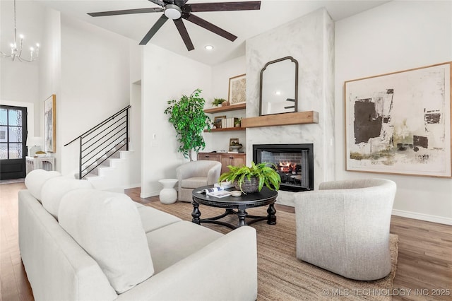living area featuring baseboards, a high end fireplace, ceiling fan with notable chandelier, wood finished floors, and stairs
