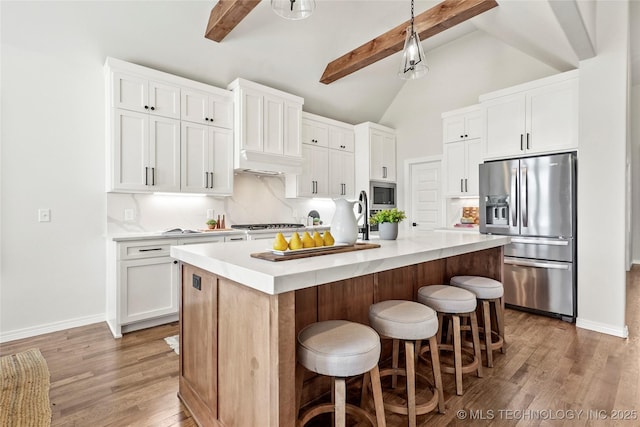 kitchen with a kitchen breakfast bar, light wood-style flooring, light countertops, beamed ceiling, and appliances with stainless steel finishes