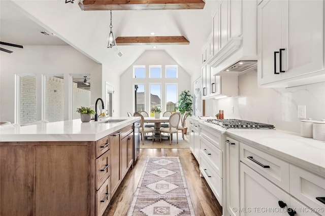 kitchen featuring a sink, a kitchen island with sink, brown cabinets, beamed ceiling, and light wood finished floors