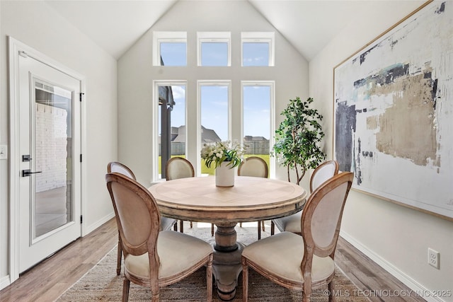 dining area with light wood-style flooring, baseboards, and lofted ceiling
