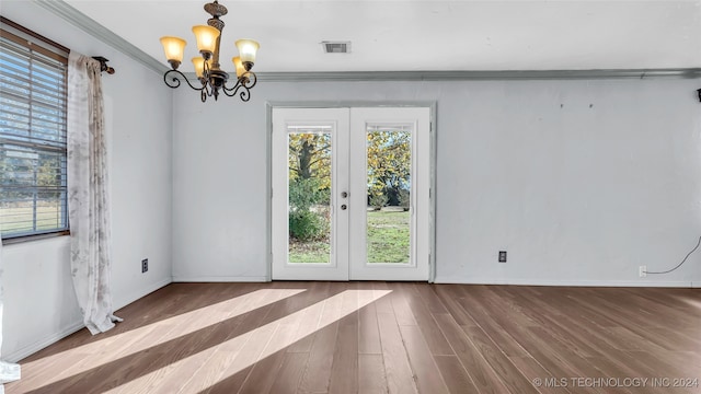 empty room featuring a notable chandelier, dark hardwood / wood-style floors, crown molding, and french doors