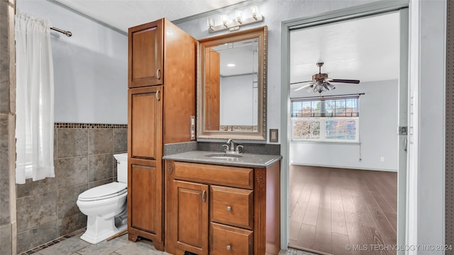 bathroom with vanity, ceiling fan, hardwood / wood-style flooring, tile walls, and toilet